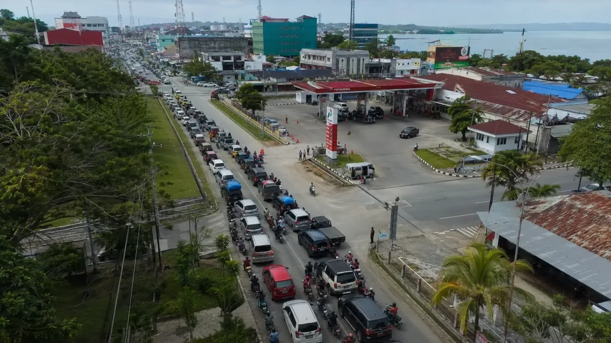 Foto udara antrean panjang kendaraan mengular di sepanjang jalan menuju sebuah SPBU Pertamina di Manokwari, dengan pemandangan kota dan teluk di latar belakang.